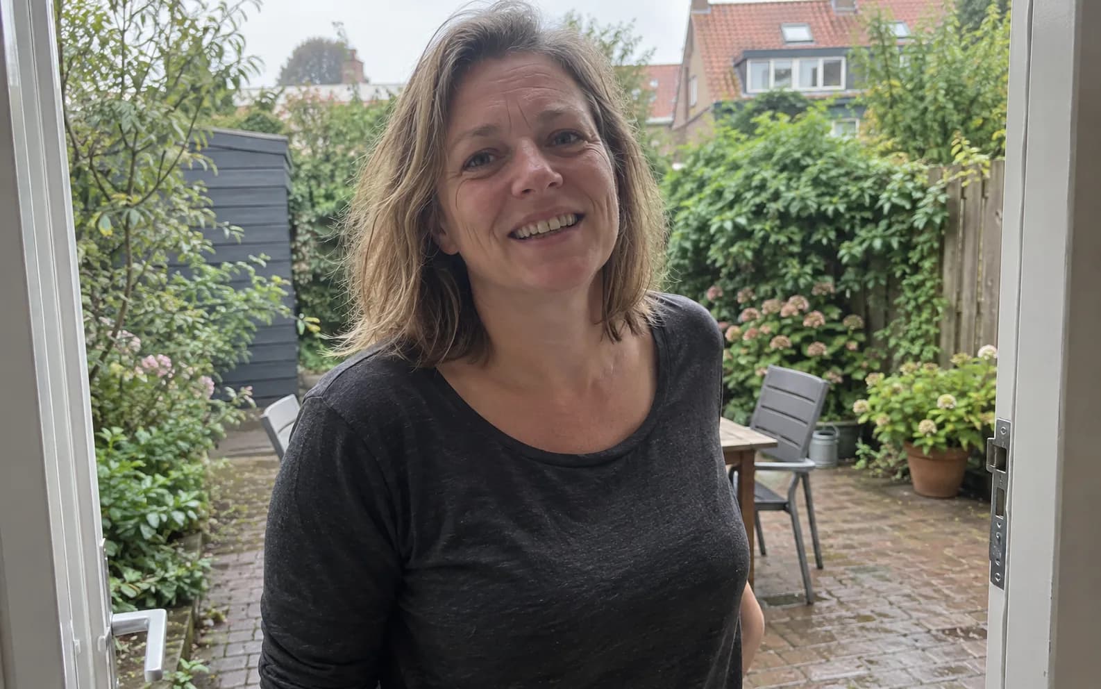 A woman smiling by the doorway to a small garden