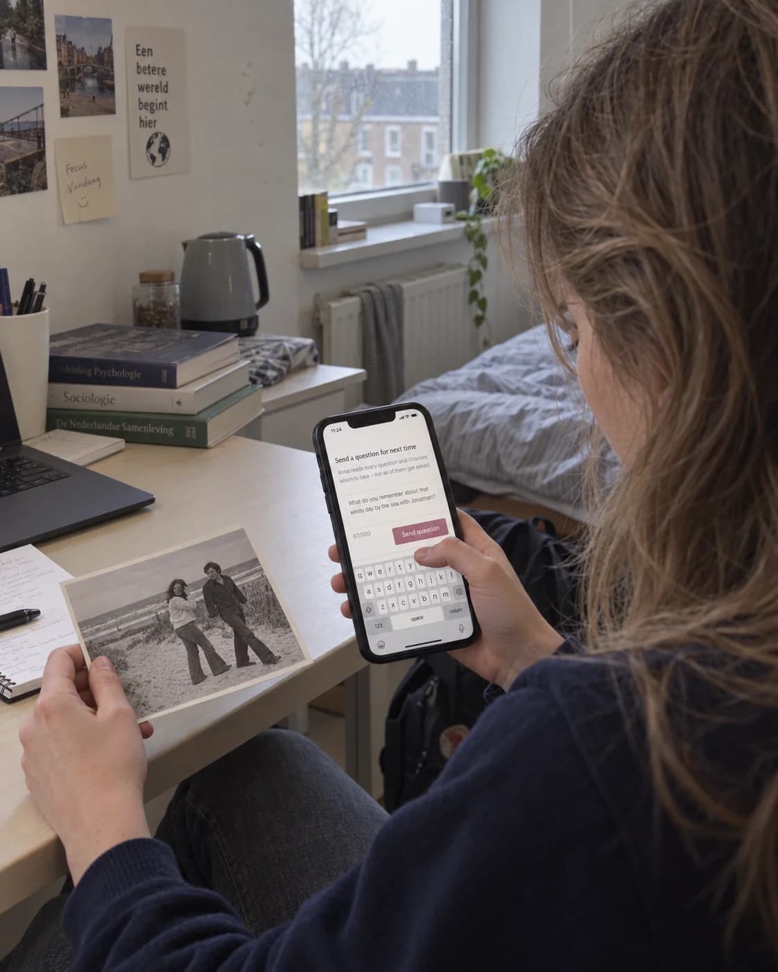 A granddaughter in her student room holds an old family photograph and asks a question on her phone.
