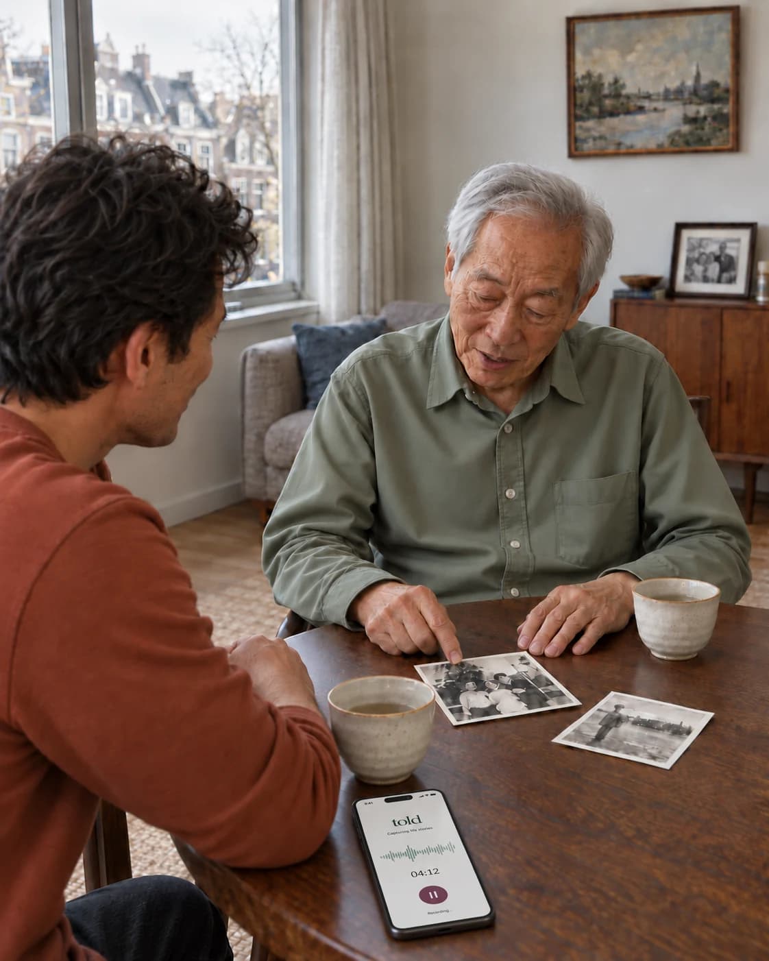 Thomas and his son talk over old family photographs while their conversation records on a phone.
